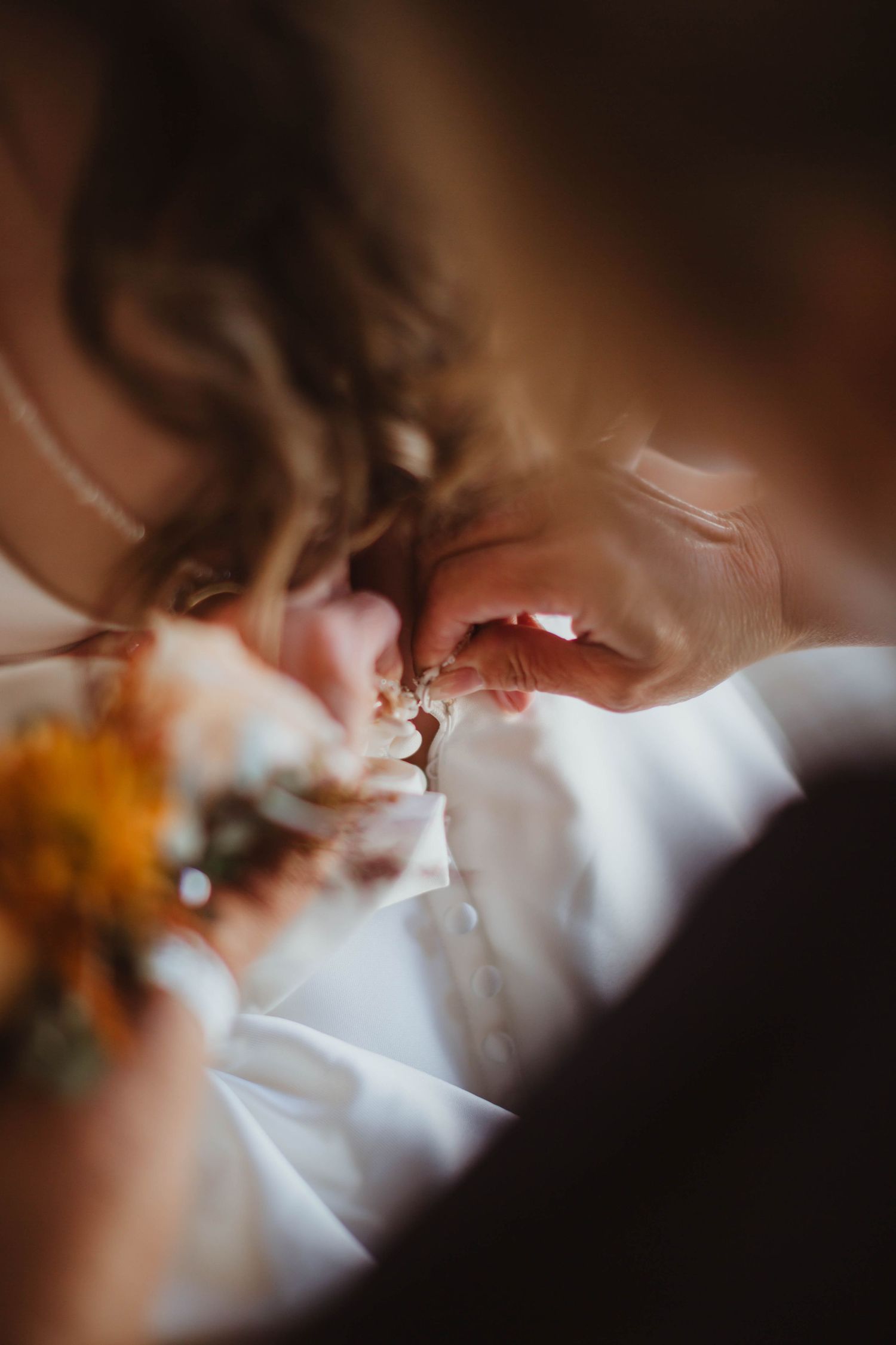 Close-up shot of someone adjusting wedding dress details with orange flowers visible in frame.