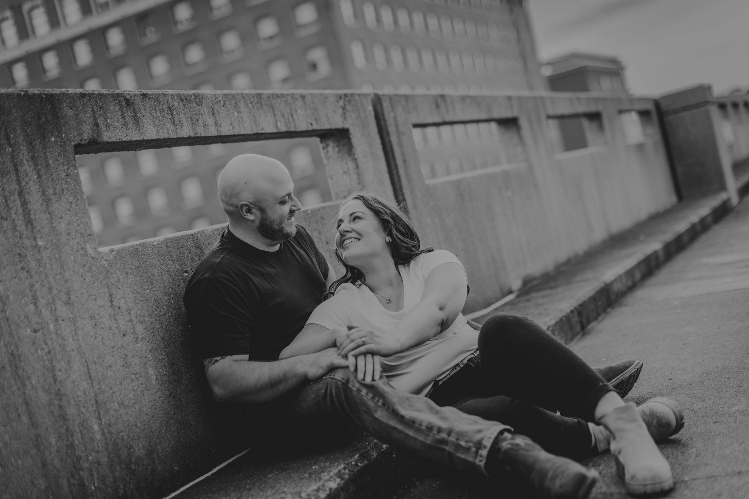 An intimate black and white portrait of a couple resting against a concrete wall in an urban setting.