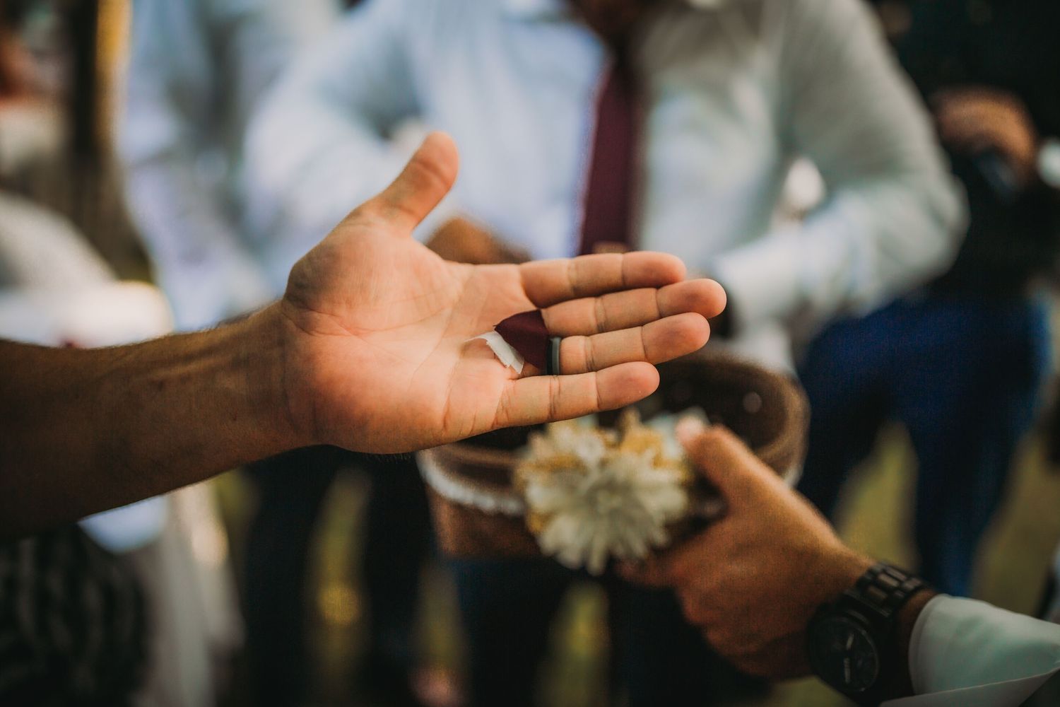 Extended open palm during outdoor event with people in formal attire in background.