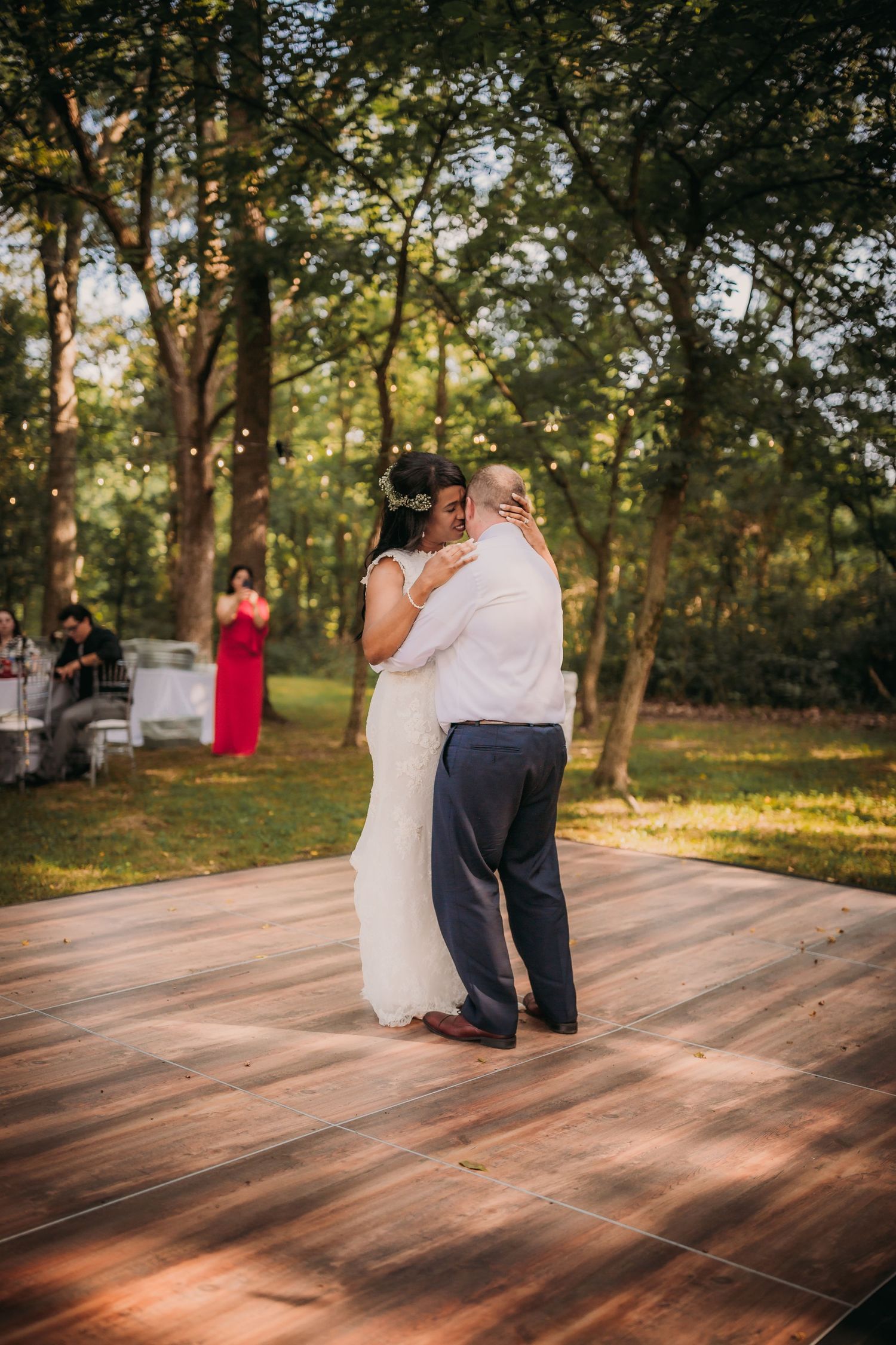 A couple dances close together on a wooden dance floor with forest scenery and golden sunlight.