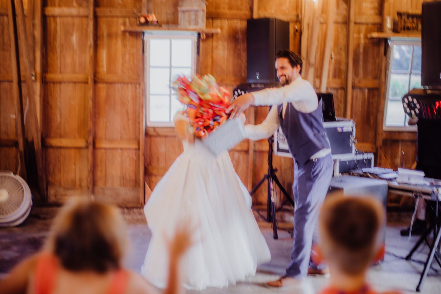 Wedding party energetically dancing at a barn reception with festive lighting.