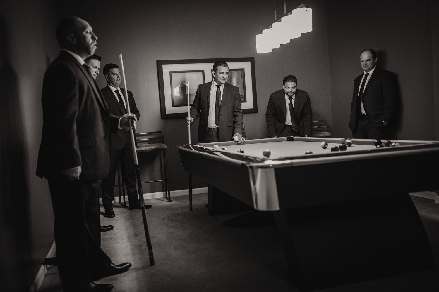 A black and white image of people playing pool in a dimly lit room with formal attire.