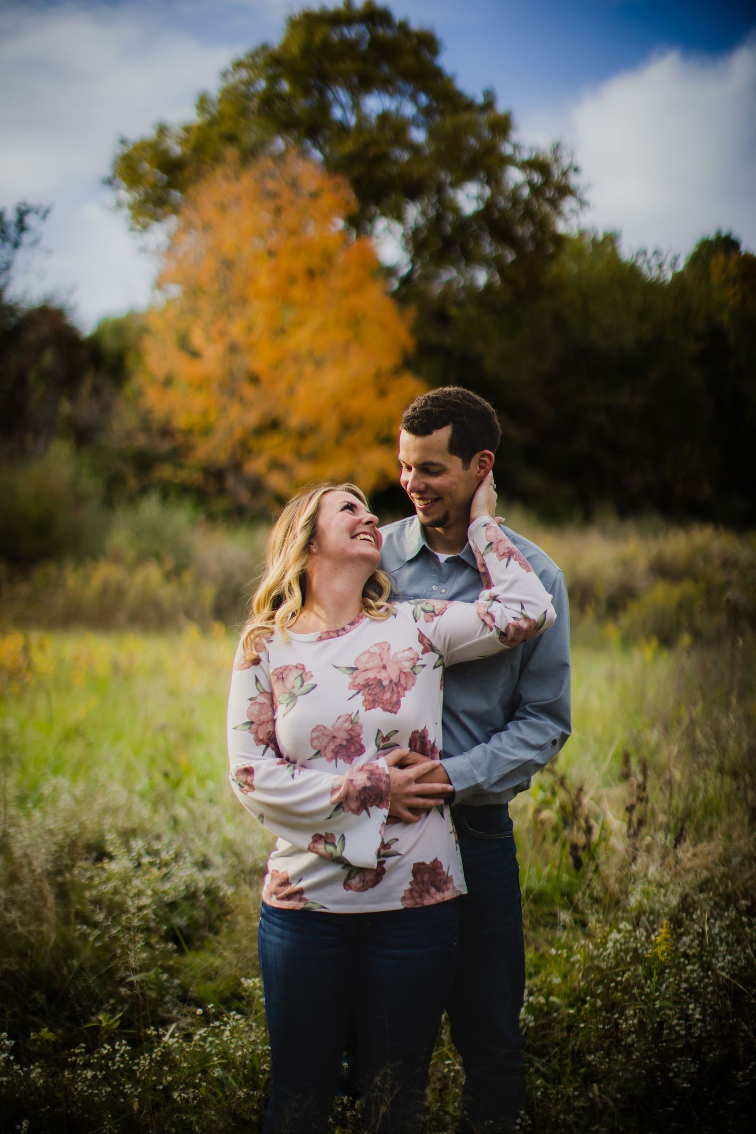 A romantic autumn portrait of a couple laughing together in a field with fall foliage.