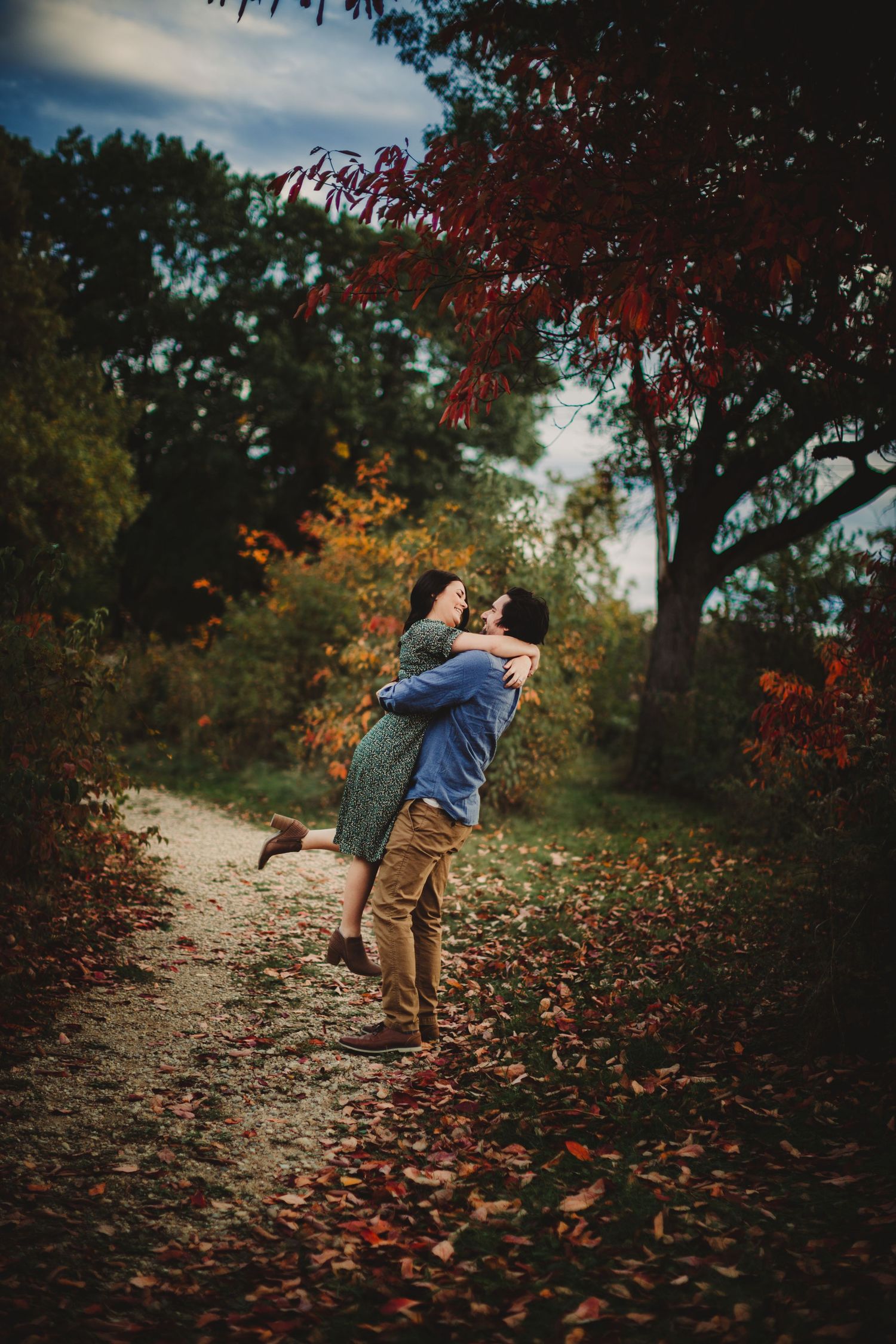 Romantic autumn scene with couple embracing on leaf-covered forest path.