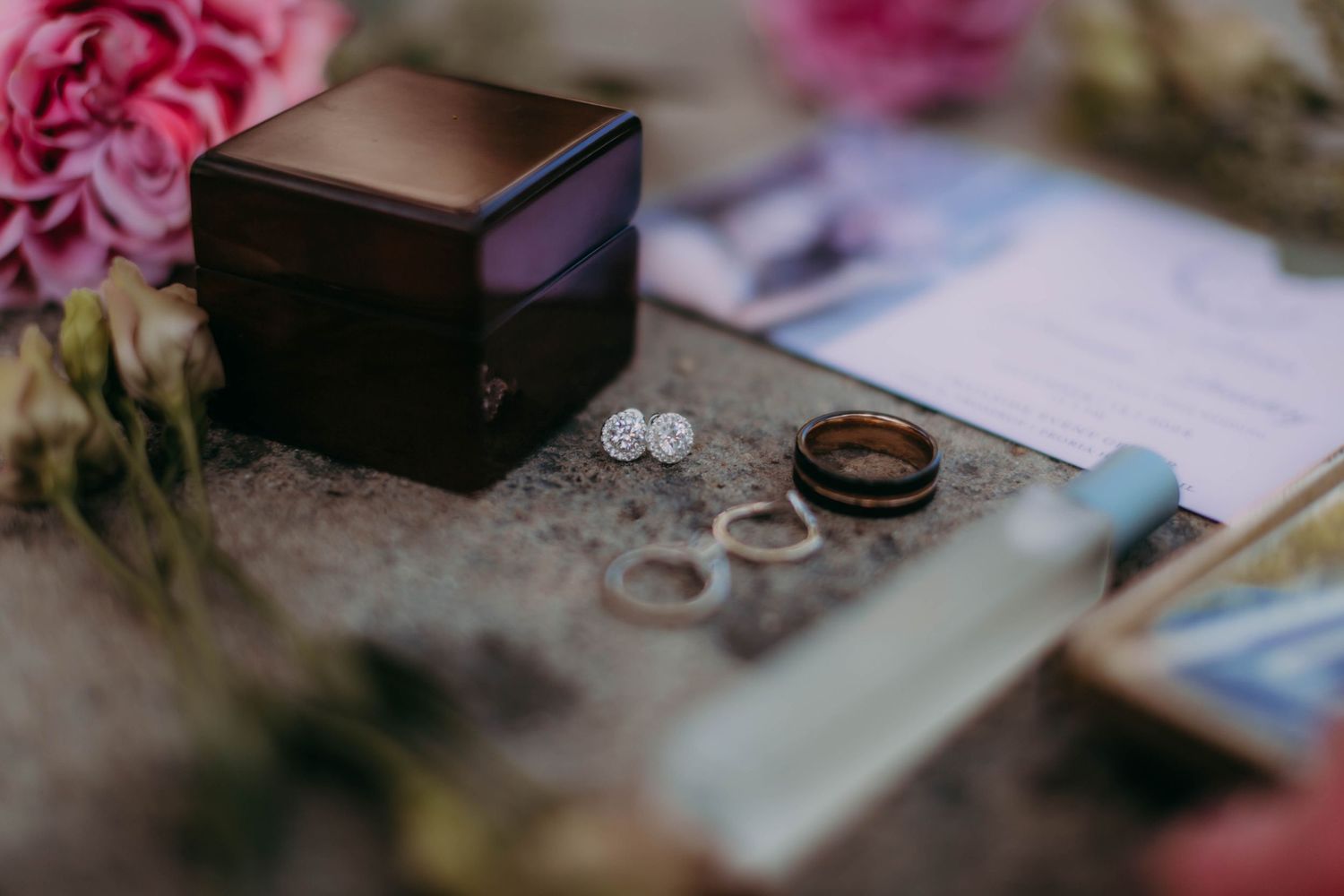 Close up of wedding rings and wooden box surrounded by soft pink roses and paper.