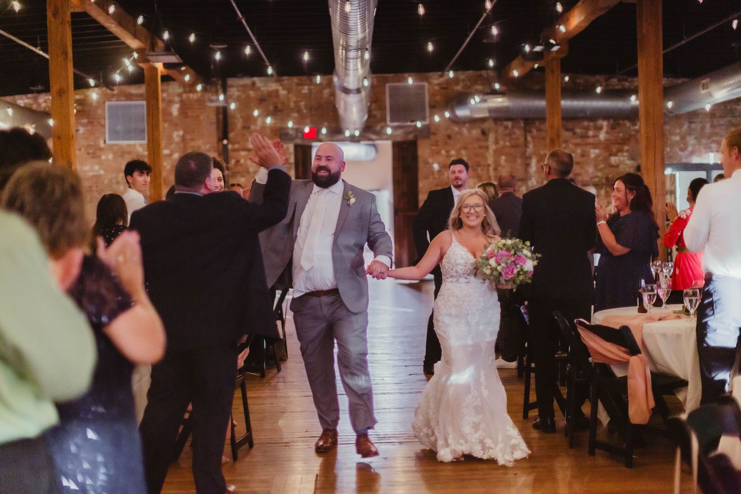 Wedding reception showing couples dancing under string lights in rustic brick venue.