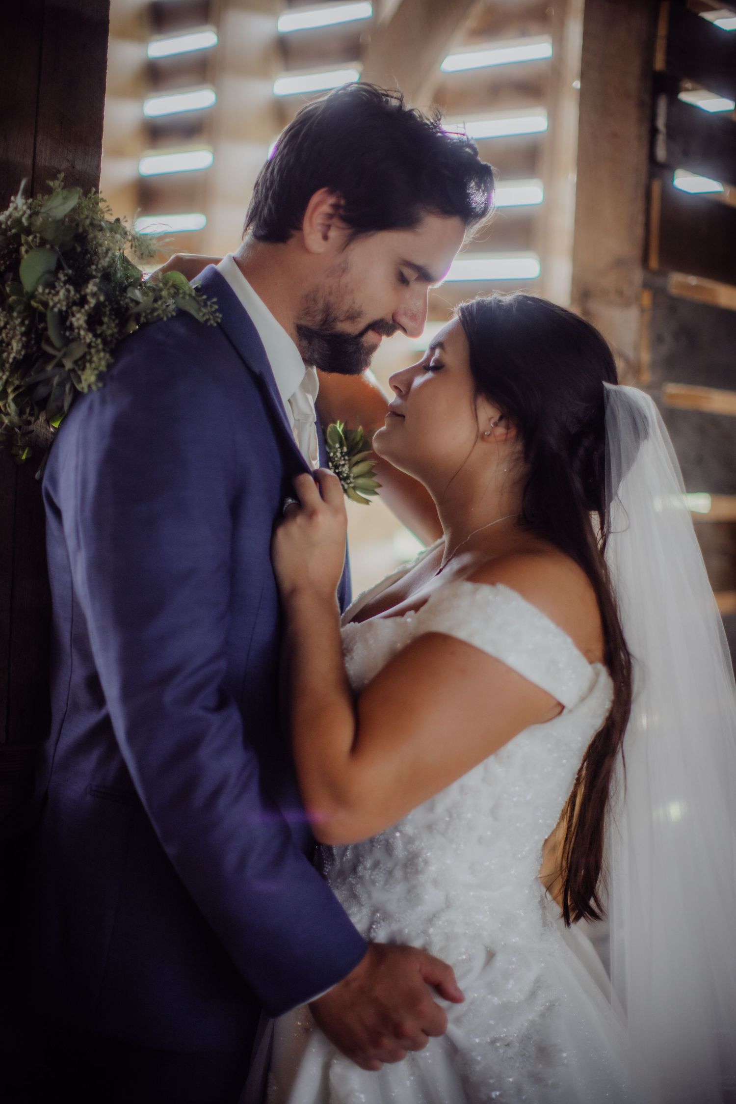 Romantic wedding kiss captured in a rustic barn with beautiful natural lighting streaming through.