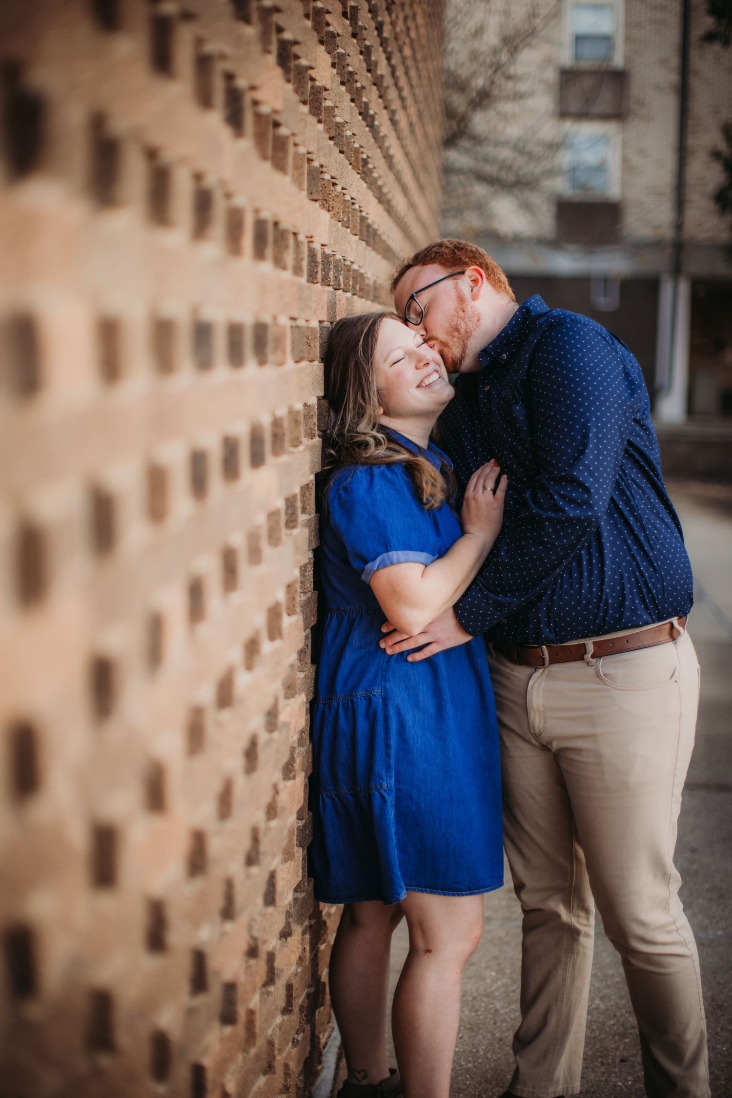 A couple laughs together while leaning against a unique architectural wall with repeating indentations.