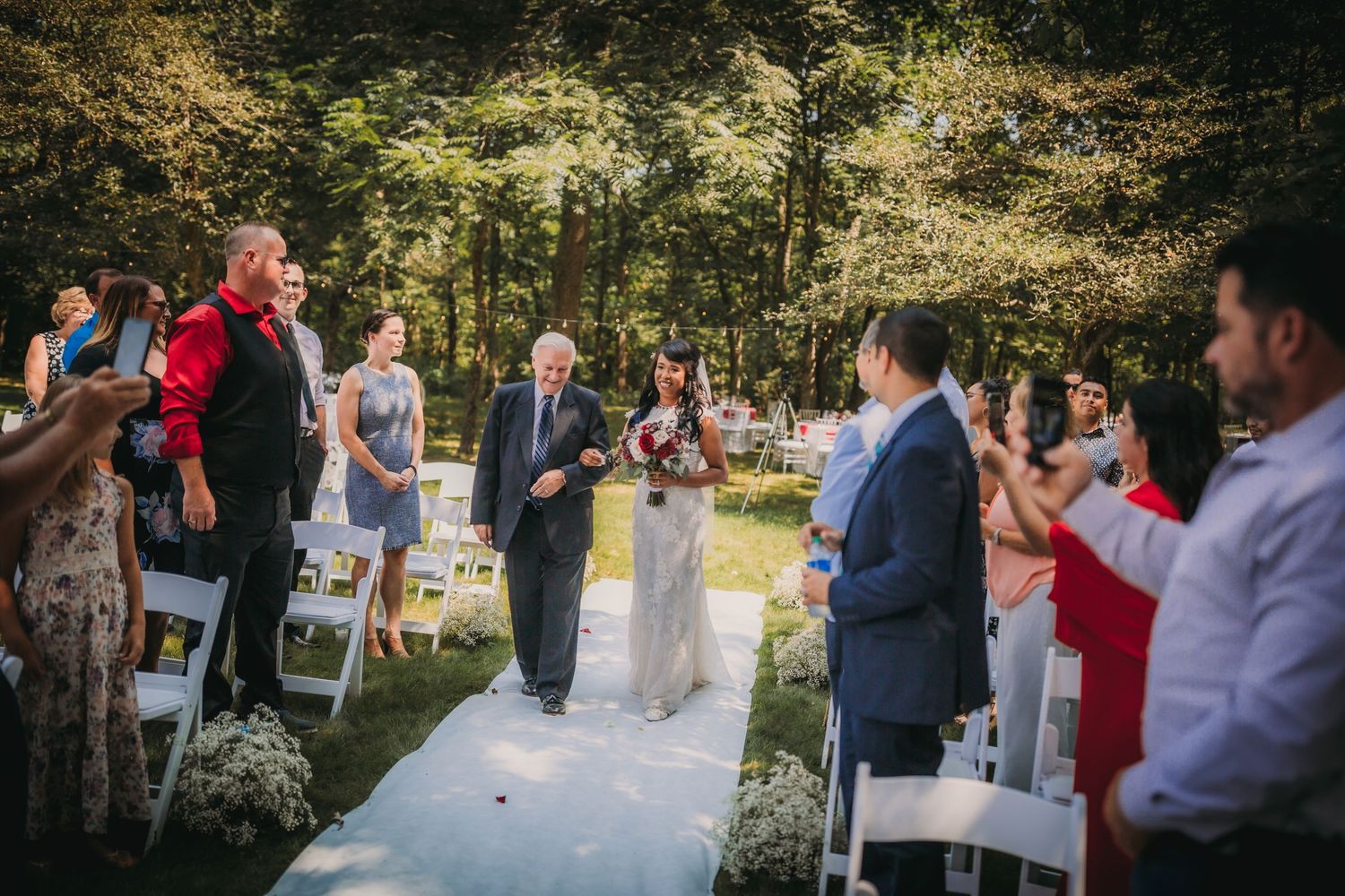 Beautiful garden wedding ceremony with guests gathered under trees on a sunny afternoon.