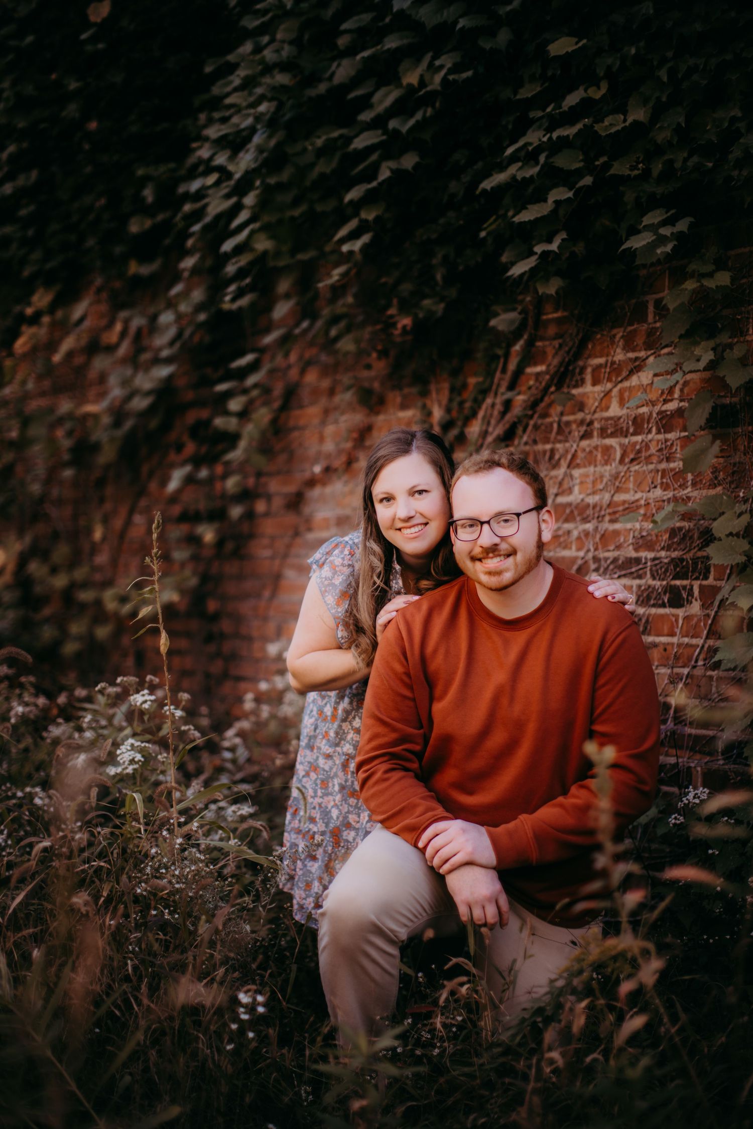 Casual outdoor portrait session featuring a couple sitting by an ivy-covered wall.