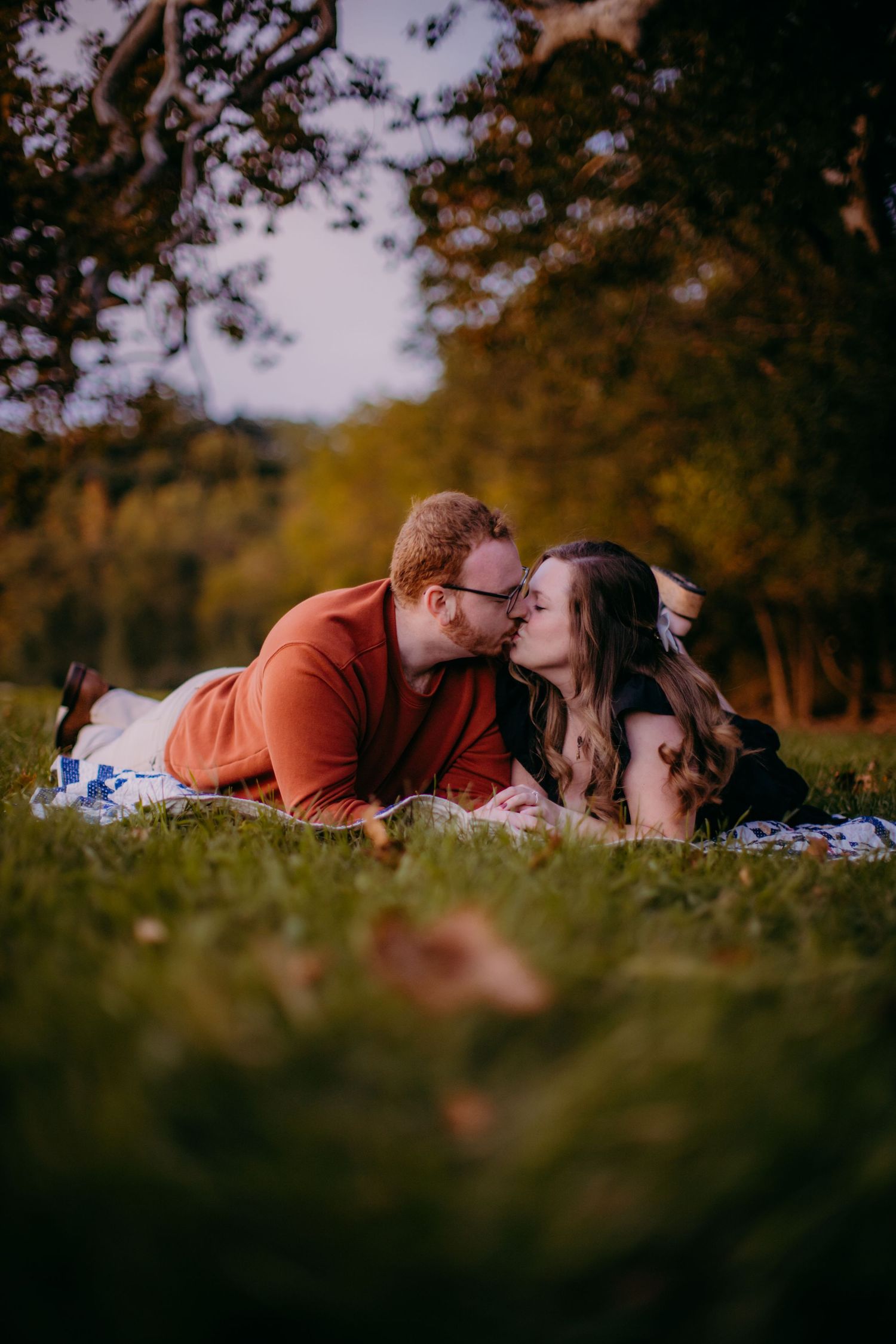 Romantic couple lying on a blanket sharing an intimate moment in autumn nature setting.