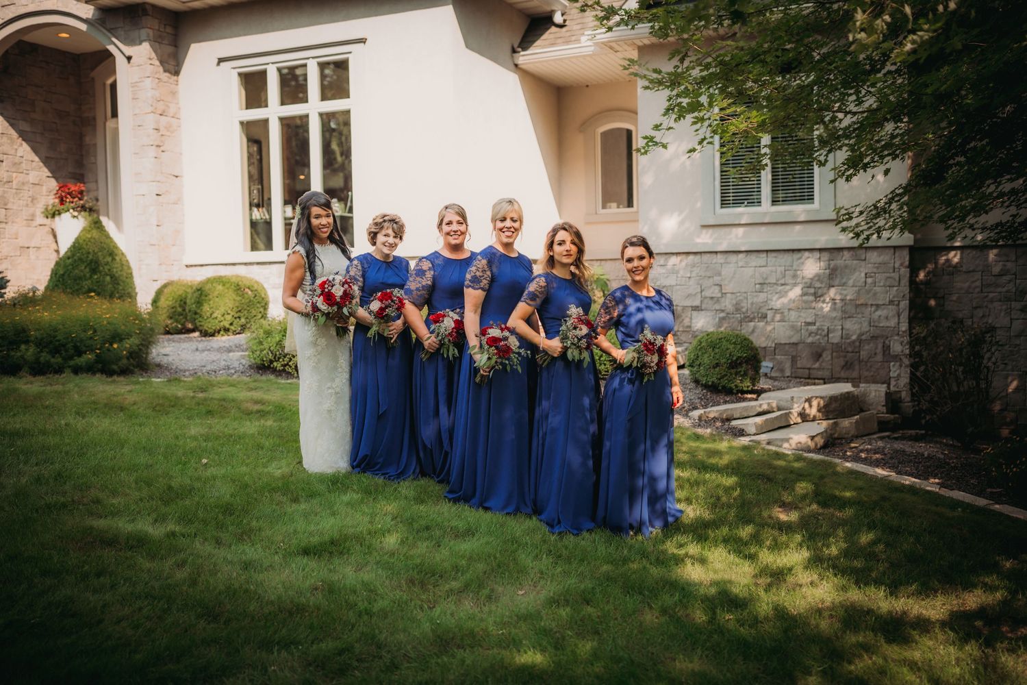 Bridesmaids in blue dresses pose together outside a stone building.
