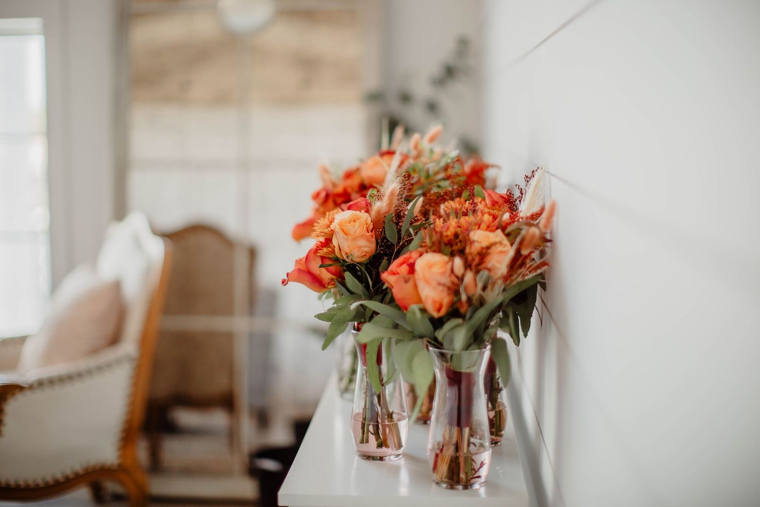 Bright coral rose bouquets in glass vases displayed against white interior decor.