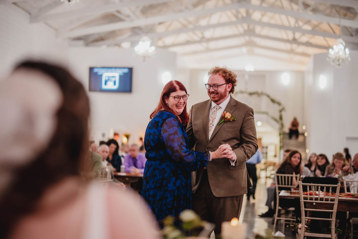 A couple shares a joyful moment while dancing in an elegantly decorated reception venue with twinkling lights.