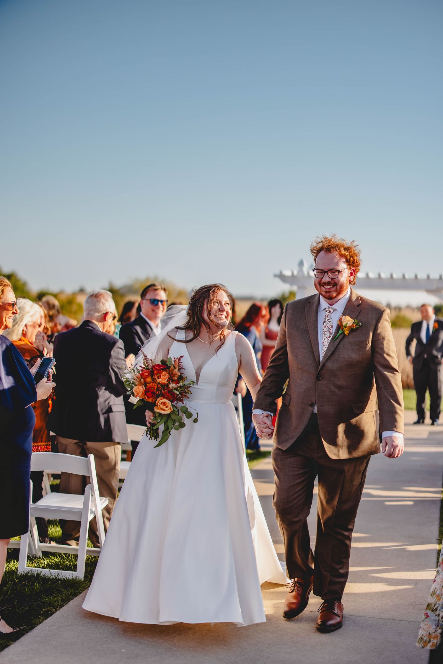 Couple walks down aisle together with autumn flowers and warm sunlight.