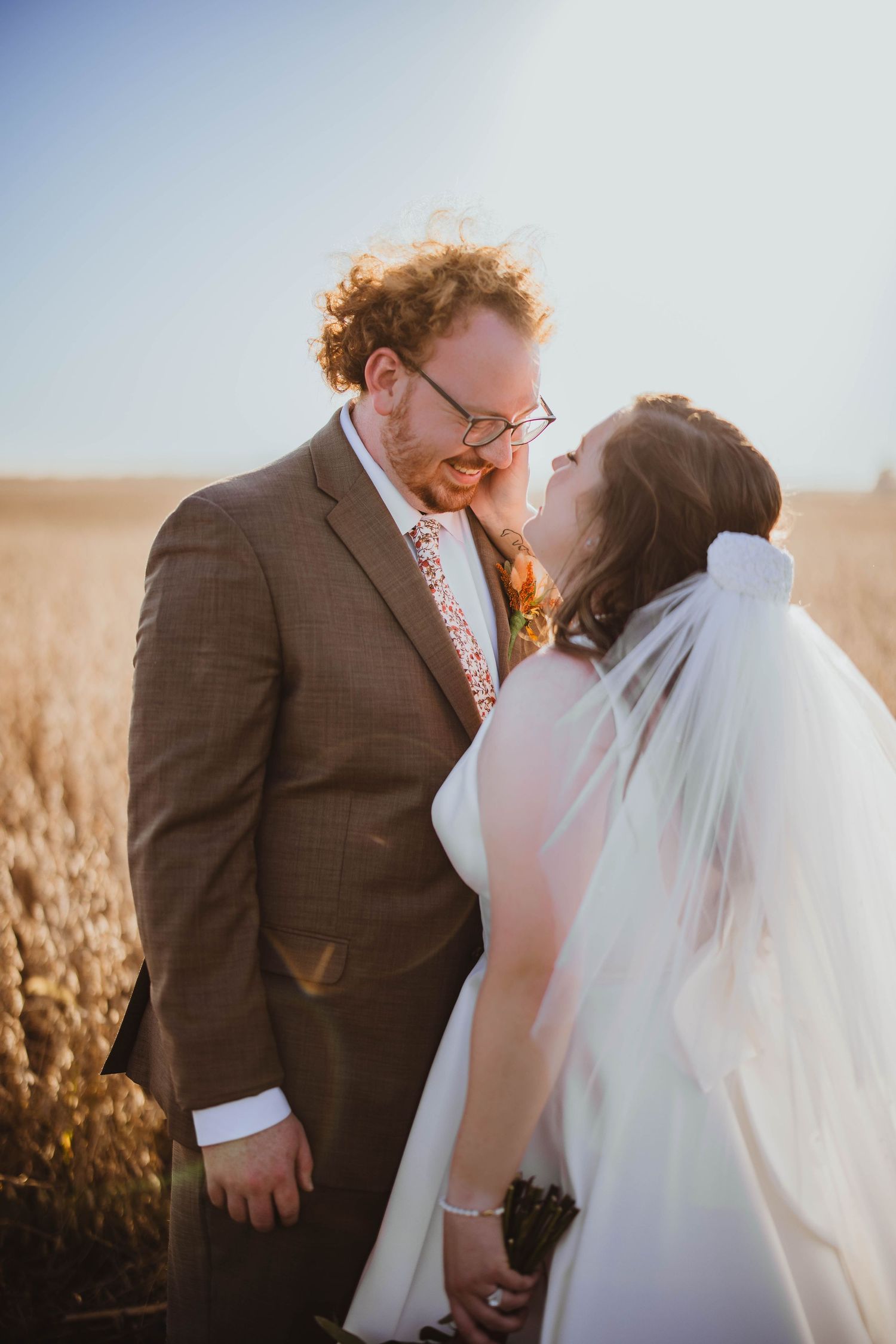 Newlywed couple sharing tender moments in a golden field at sunset during their wedding photoshoot.