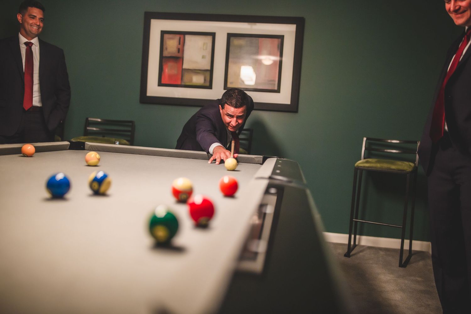 Players gathered around a pool table with colorful billiard balls scattered across the felt surface.