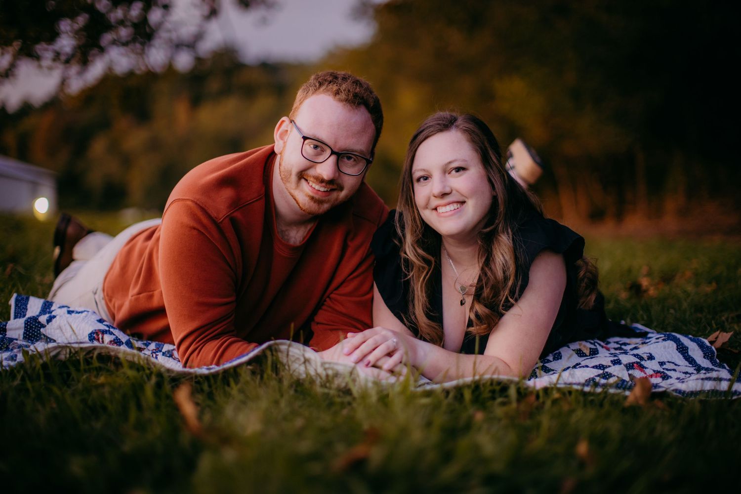 Happy couple posing on blanket outdoors during autumn portrait session.