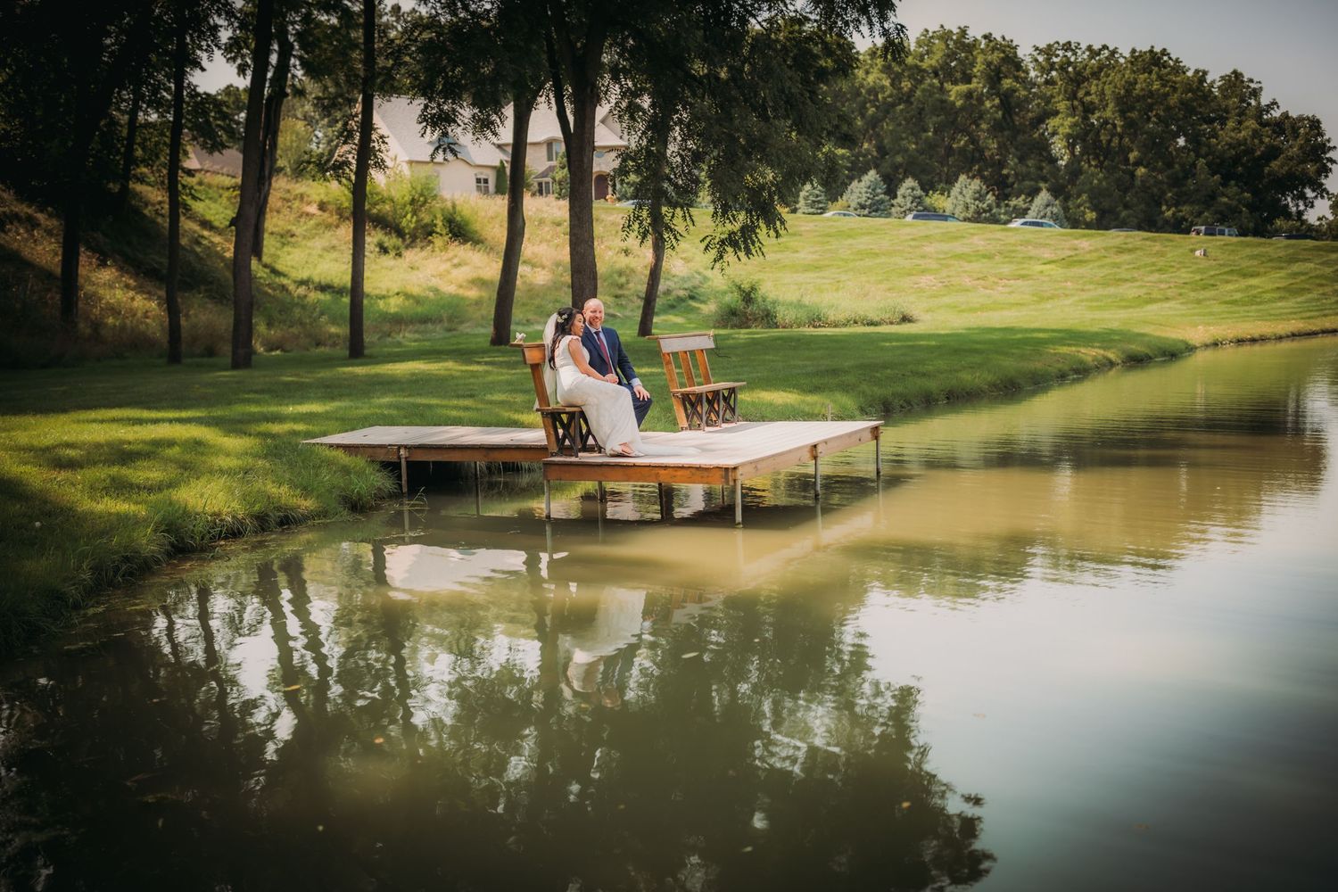 Wedding couple enjoys romantic moments near a serene pond with reflections in the water.