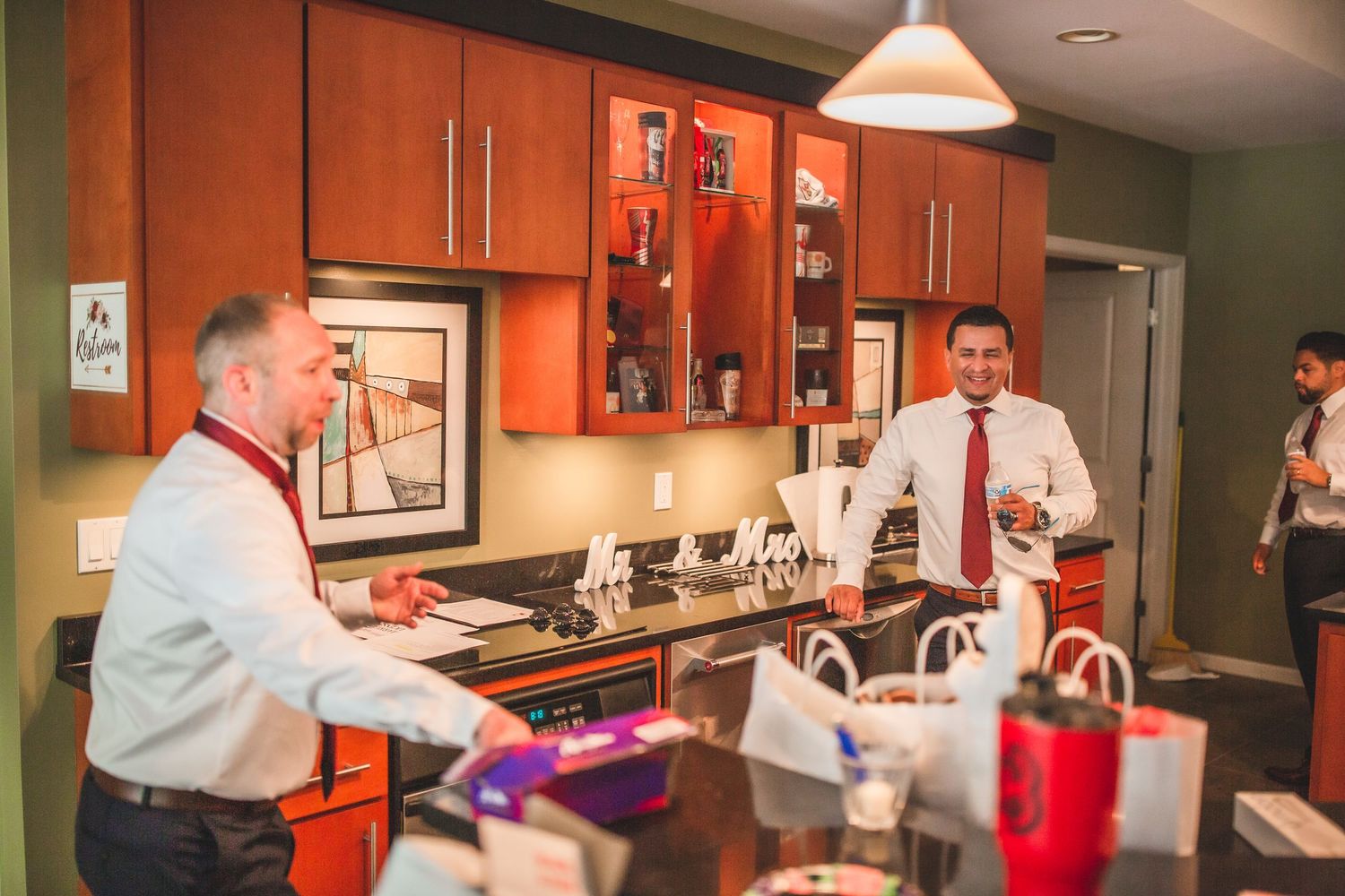 People socializing in kitchen area with wood cabinets and decorative lighting.