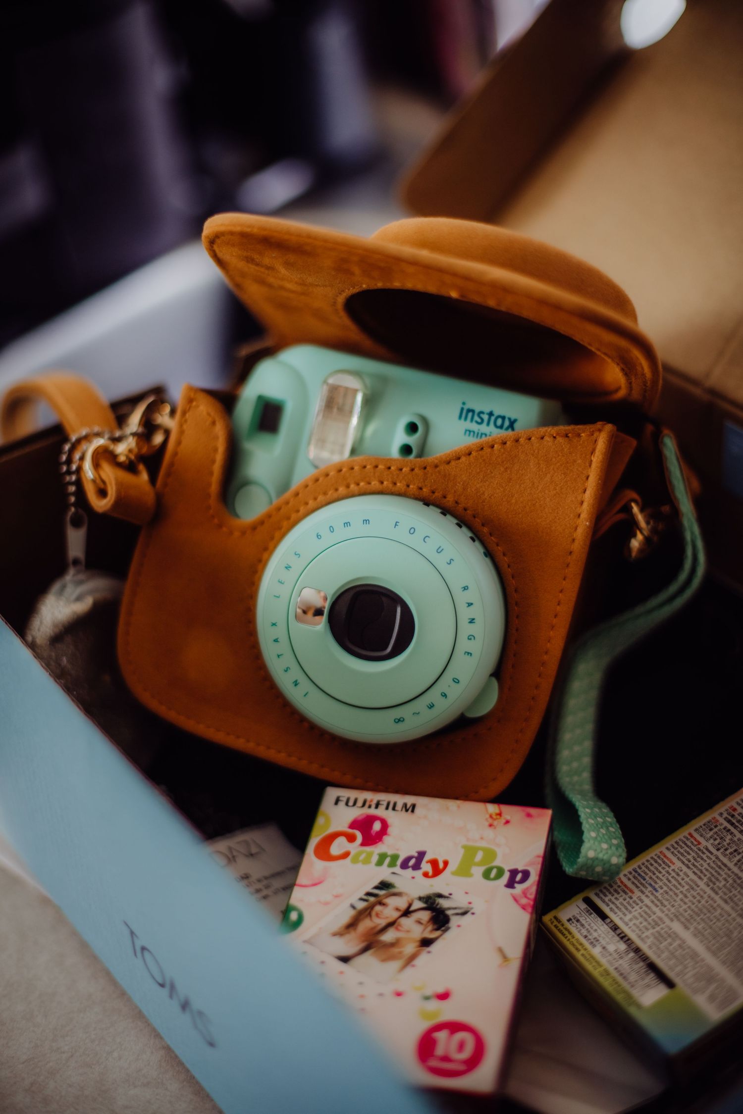 Vintage-style Fujifilm Instax camera in turquoise with brown leather case.