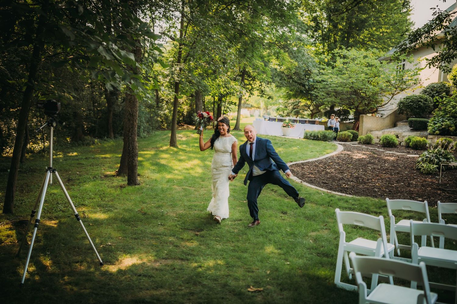 Celebrating newlyweds jump with joy on their garden ceremony aisle.