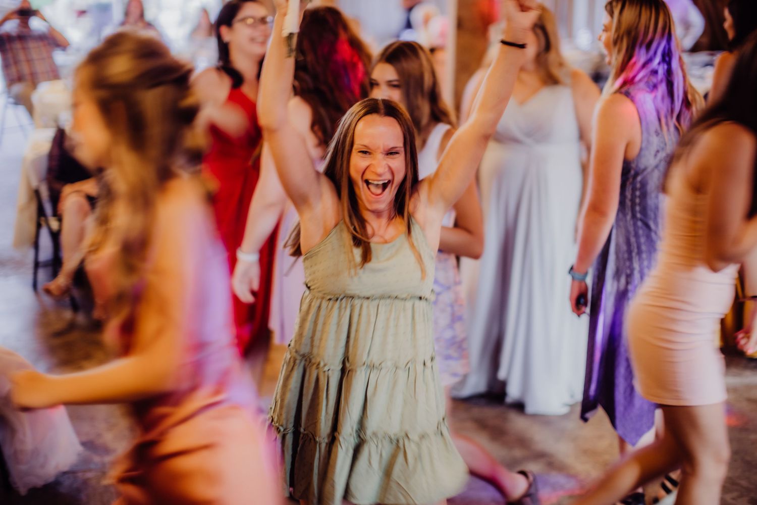 Guests dancing and celebrating at a barn wedding reception with purple and red lighting.