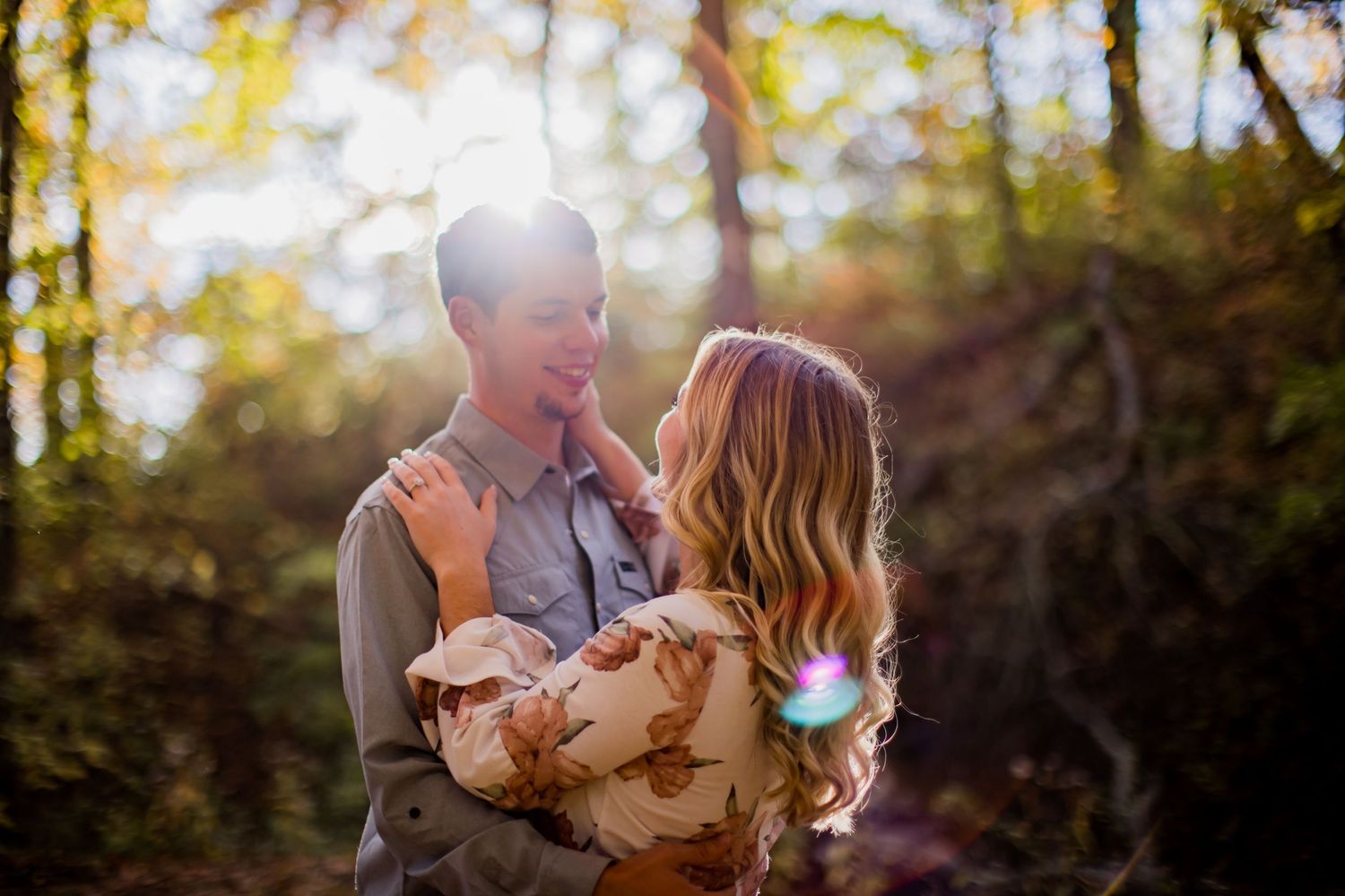 Couple embracing in sunlit forest with lens flare creating a dreamy autumn atmosphere.