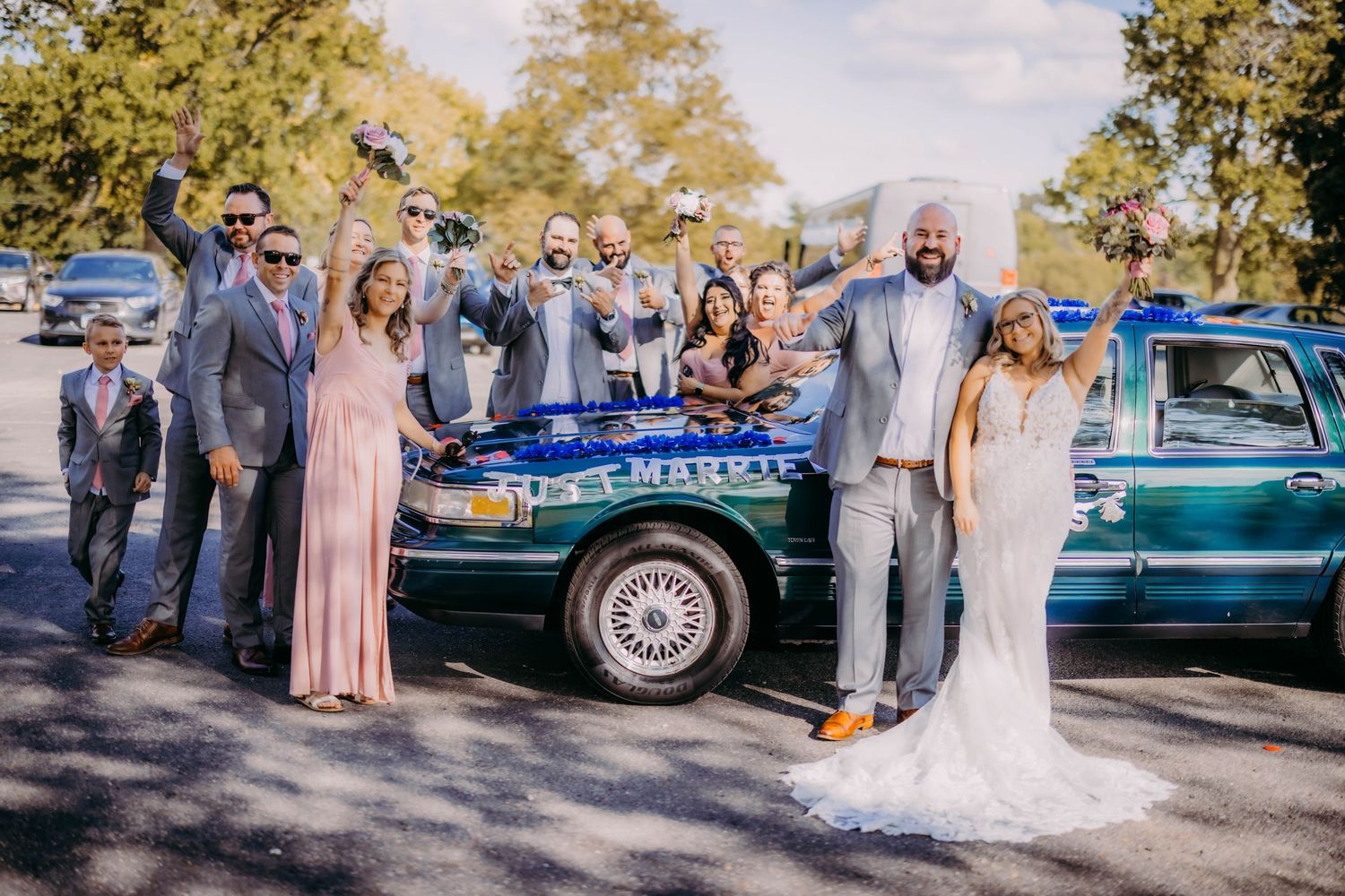 Wedding party poses with vintage car during outdoor photo session.