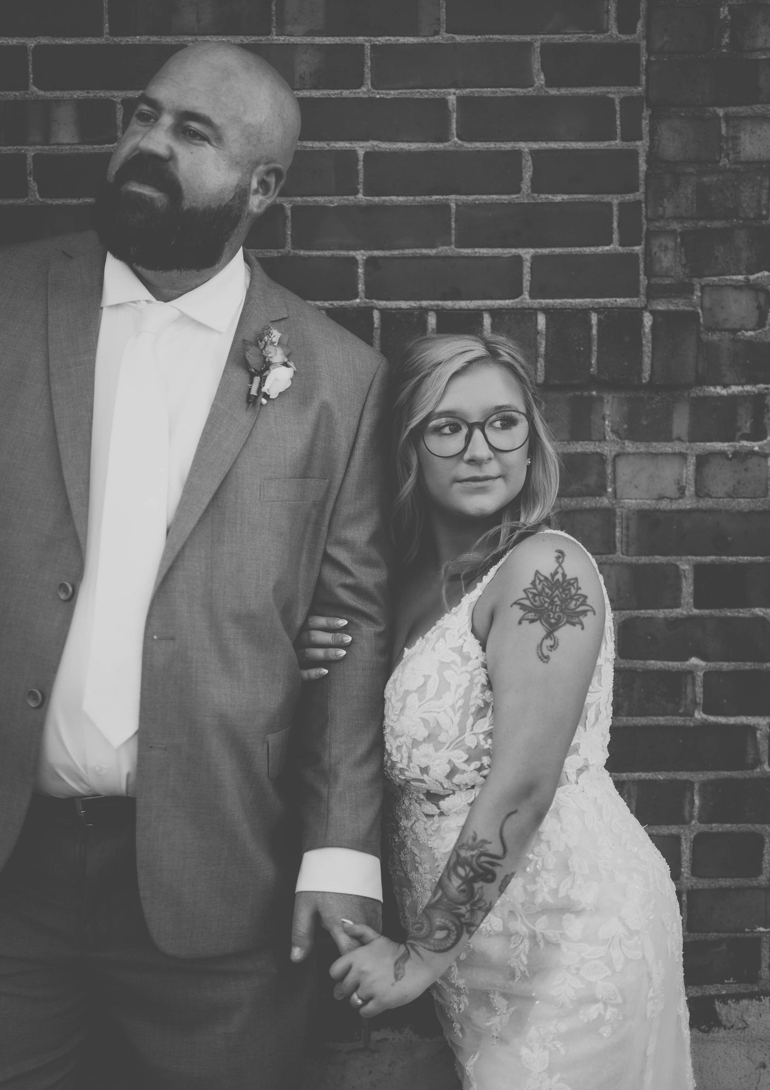 A black and white wedding portrait capturing a classic posed moment against brick architecture.