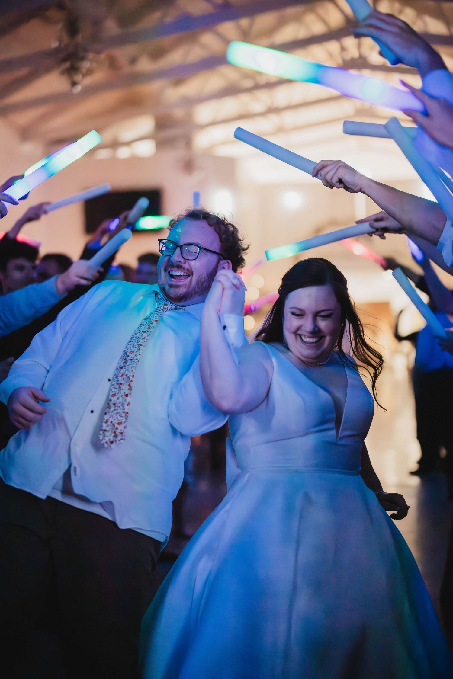 Wedding celebration with dancing couple surrounded by guests waving bright blue LED sticks.