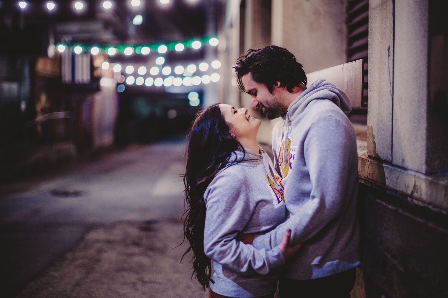 Intimate nighttime portrait of a couple kissing beneath glowing string lights.