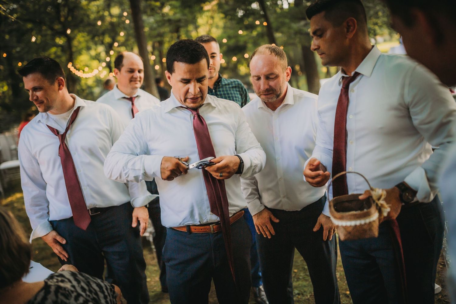 Group of men in matching white shirts and red ties gather together at outdoor event.