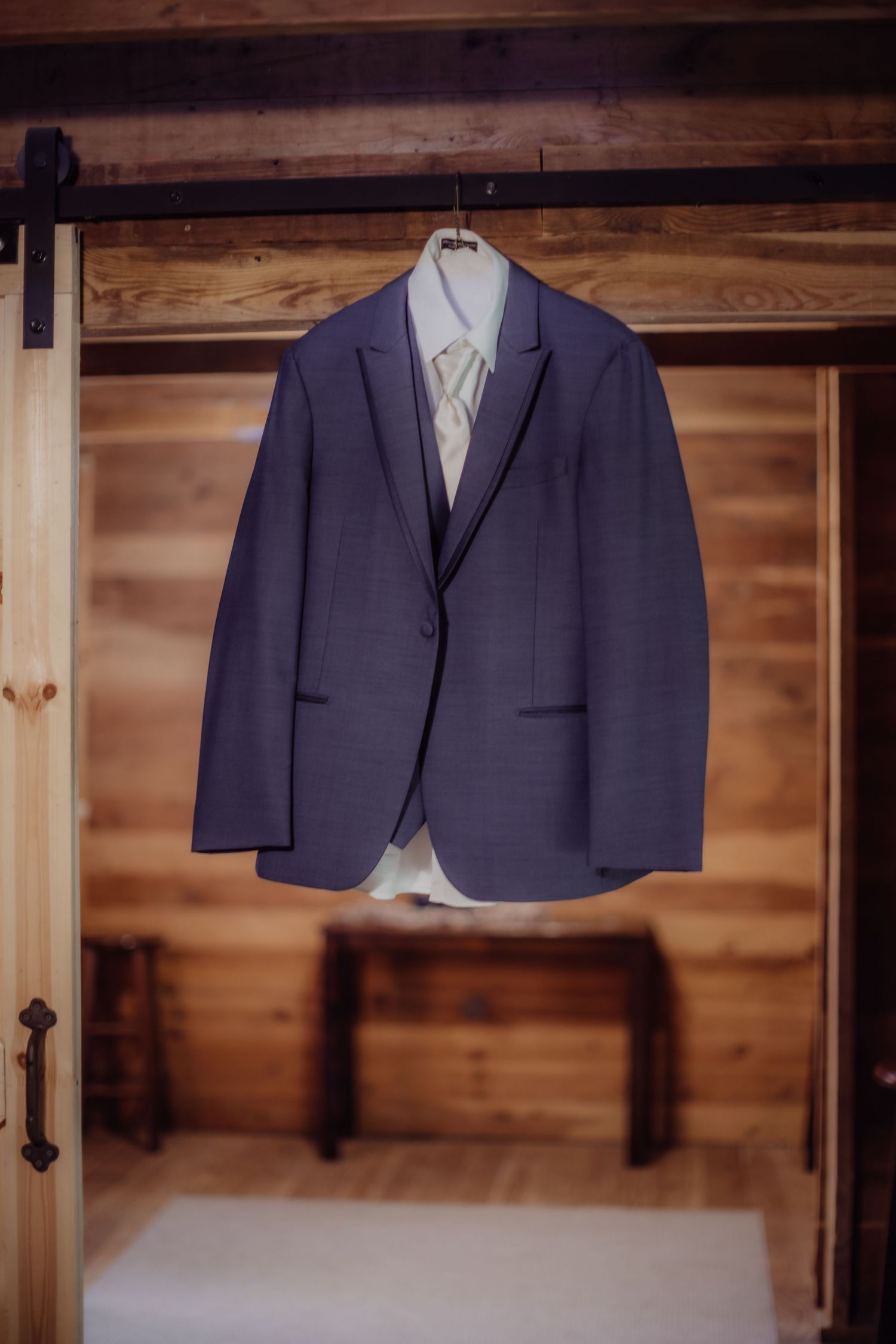 Navy blue suit jacket hanging against rustic wooden wall.