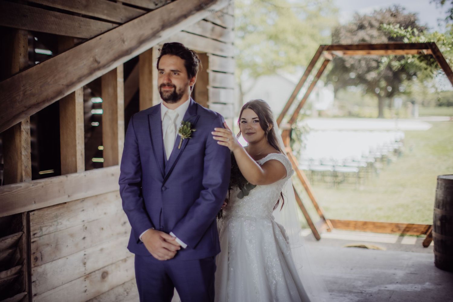 A couple has their first look moment on their wedding day in front of a rustic wooden backdrop.