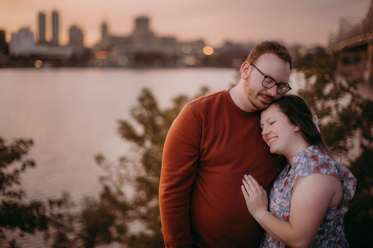 A couple shares a sweet moment against the backdrop of a sunset city waterfront.