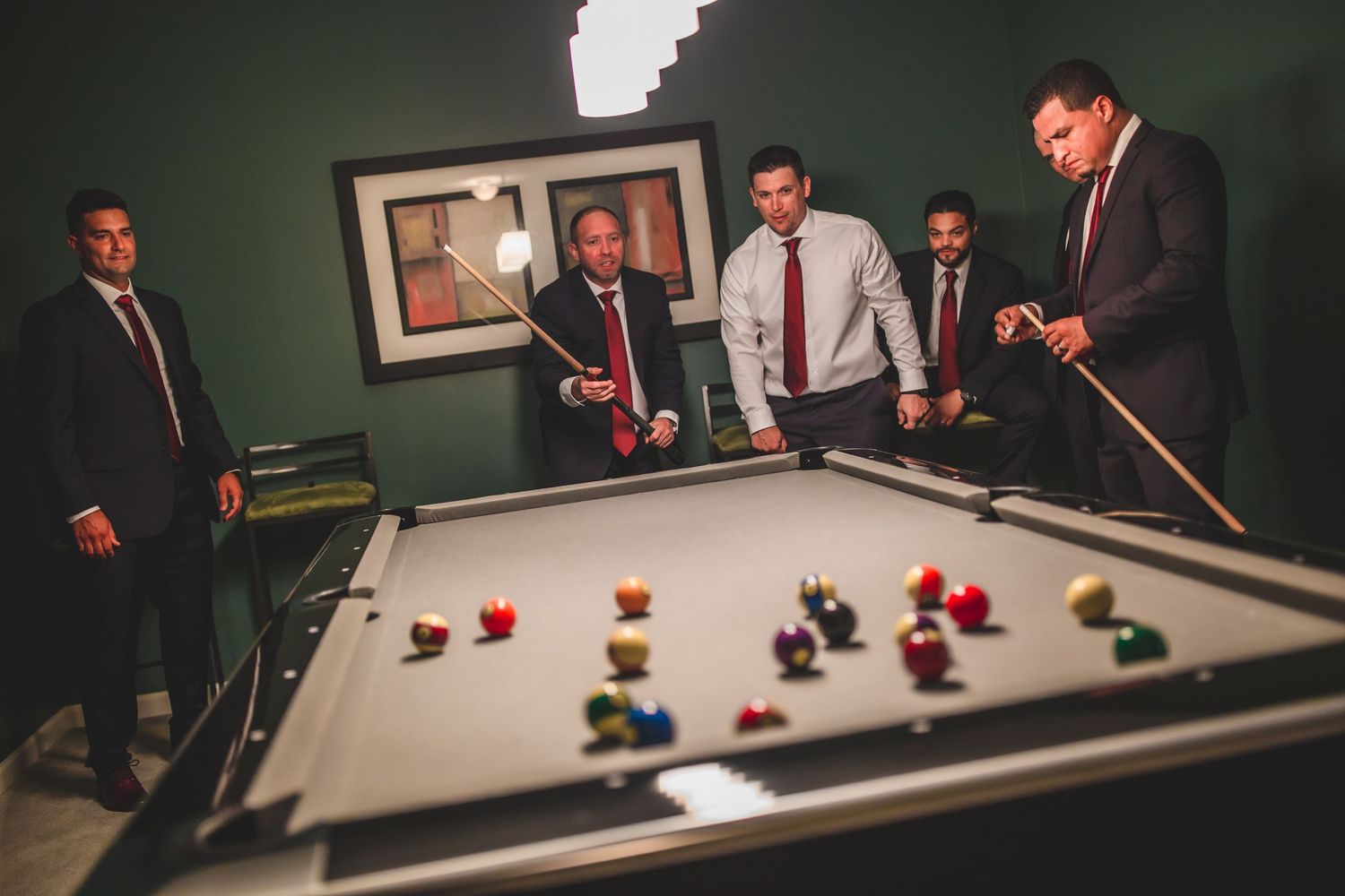 A group of formally dressed men gather around a pool table during a game in a room with green walls.