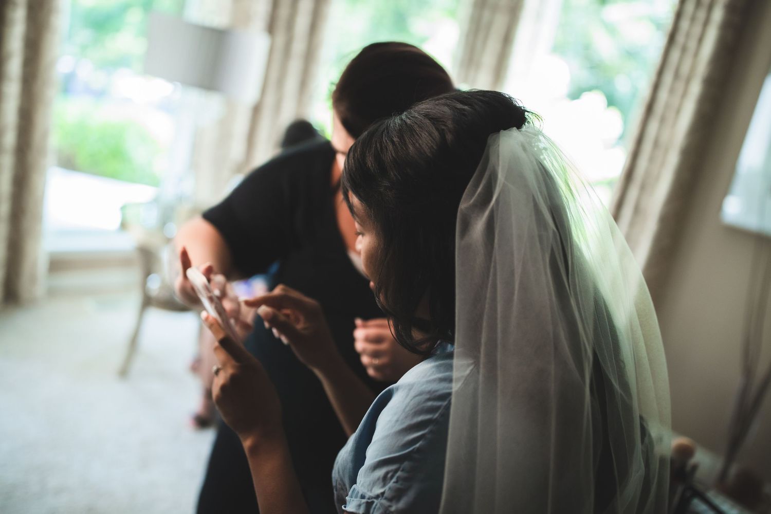 Soft focus candid moment during bridal preparations with veil and natural window light.