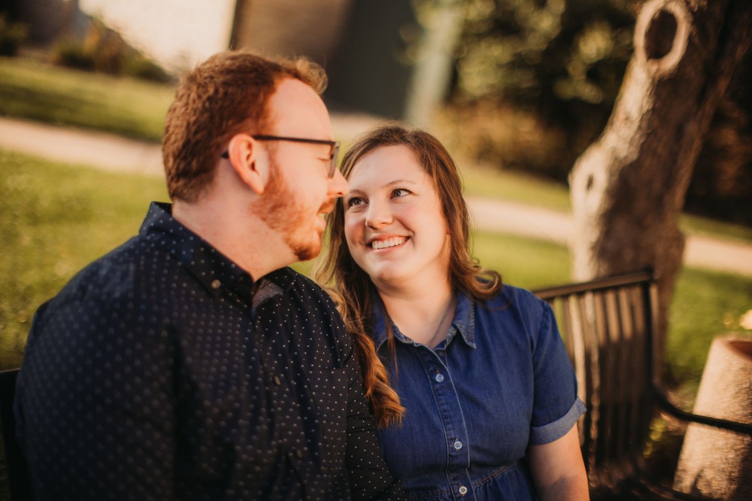 Couple sharing intimate moment while sitting on outdoor bench in warm evening light.