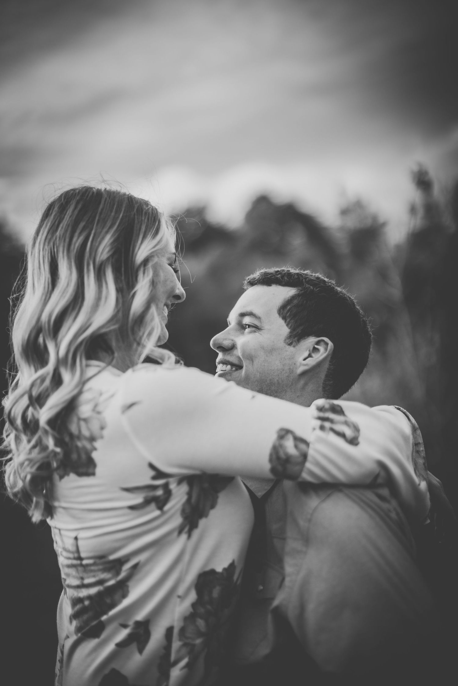 Black and white photo of a couple looking at each other lovingly while embracing outdoors.