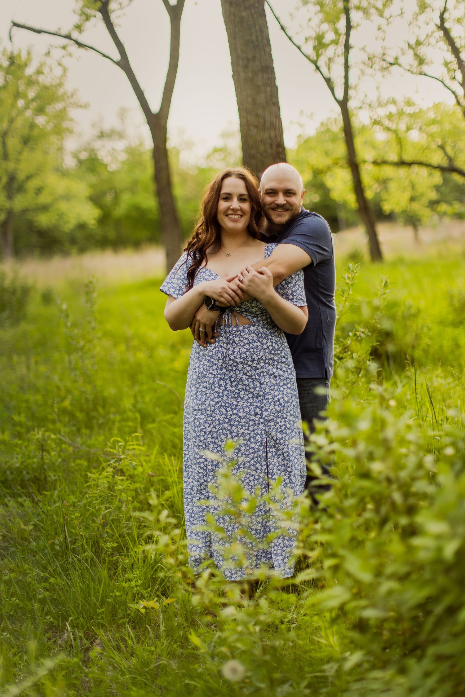 Couple embraces among wildflowers and trees during outdoor spring photo session.