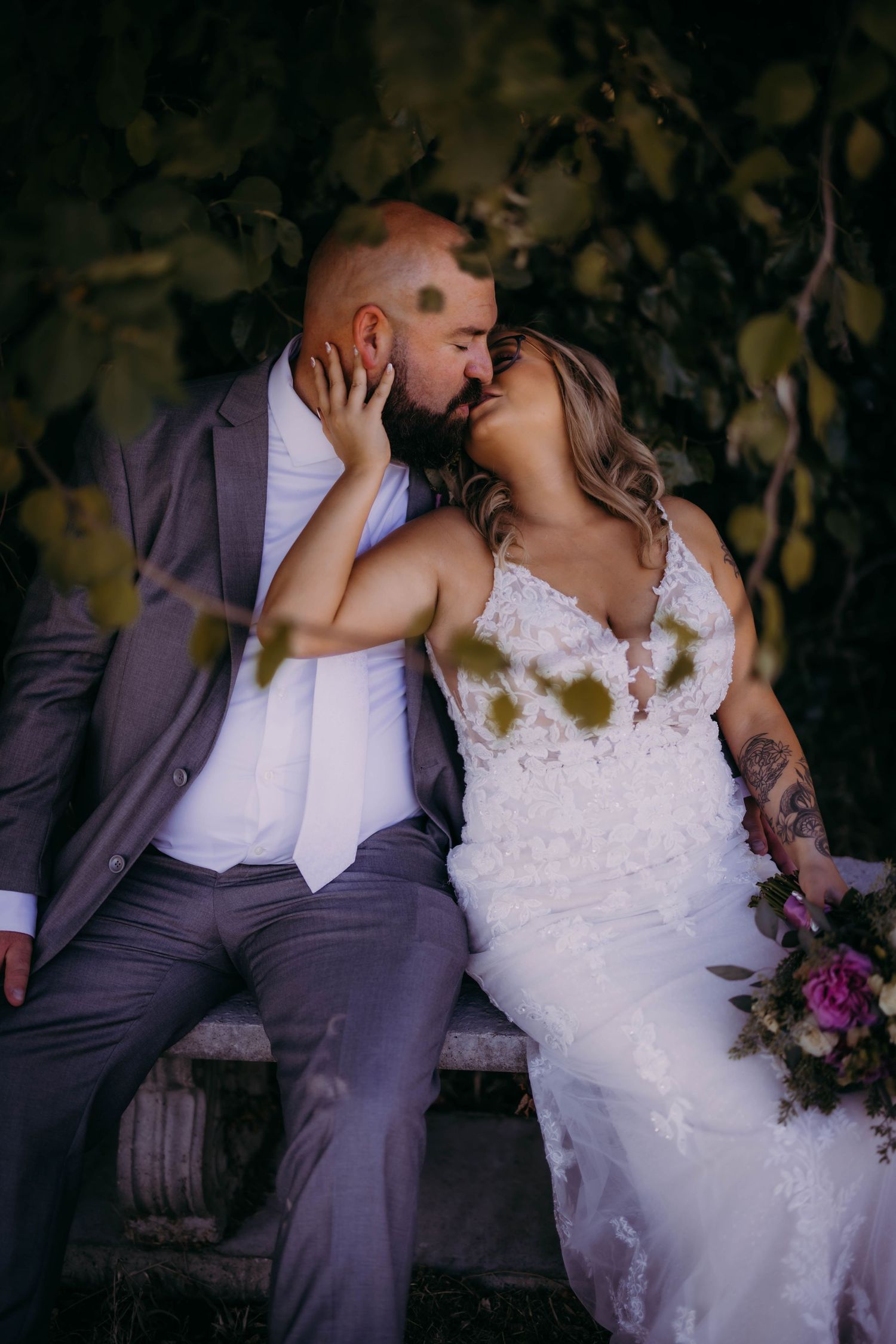 An intimate wedding portrait of a couple sharing a romantic kiss on a rustic bench.
