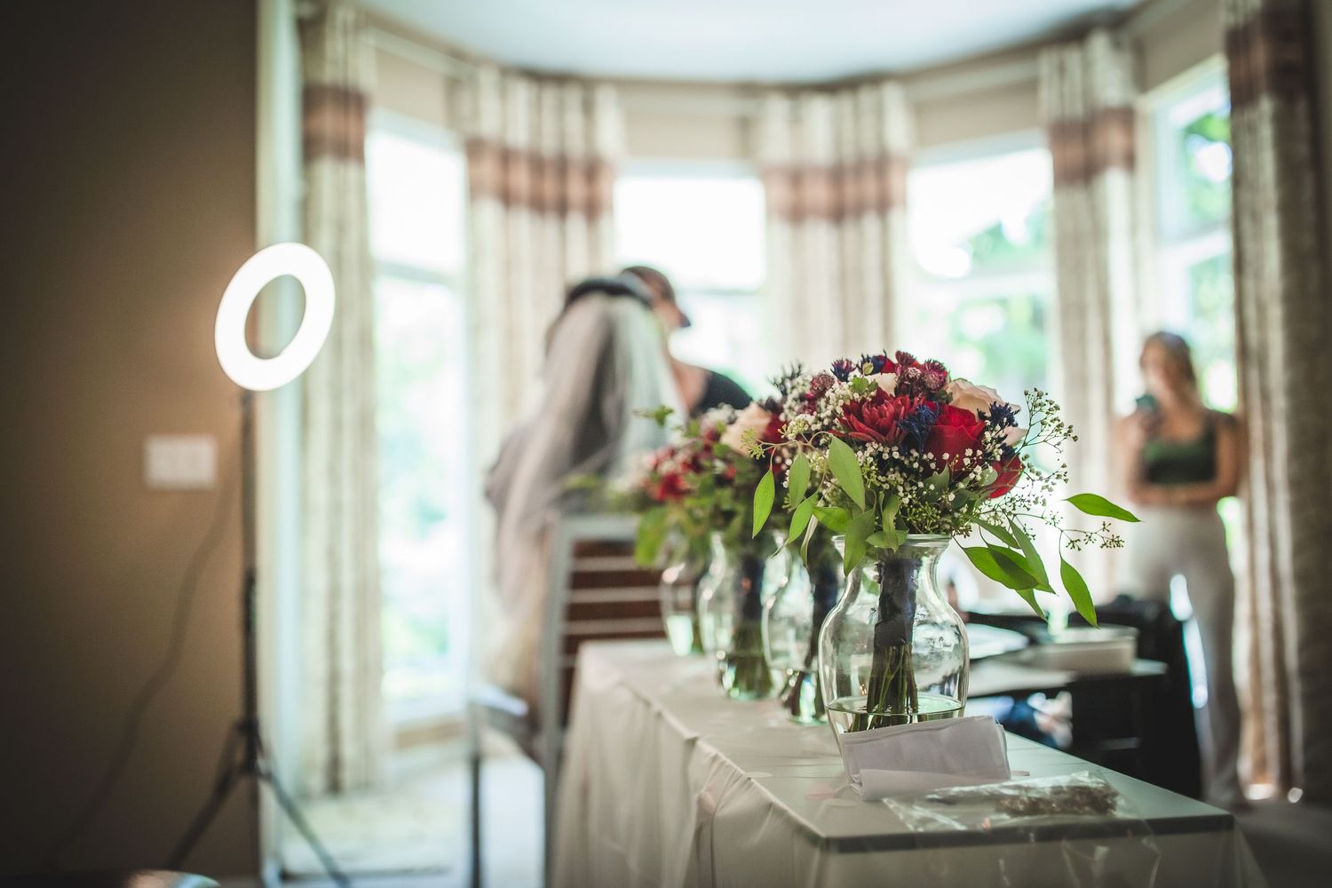 Elegant floral centerpiece with red flowers in glass vase on table during wedding preparations.