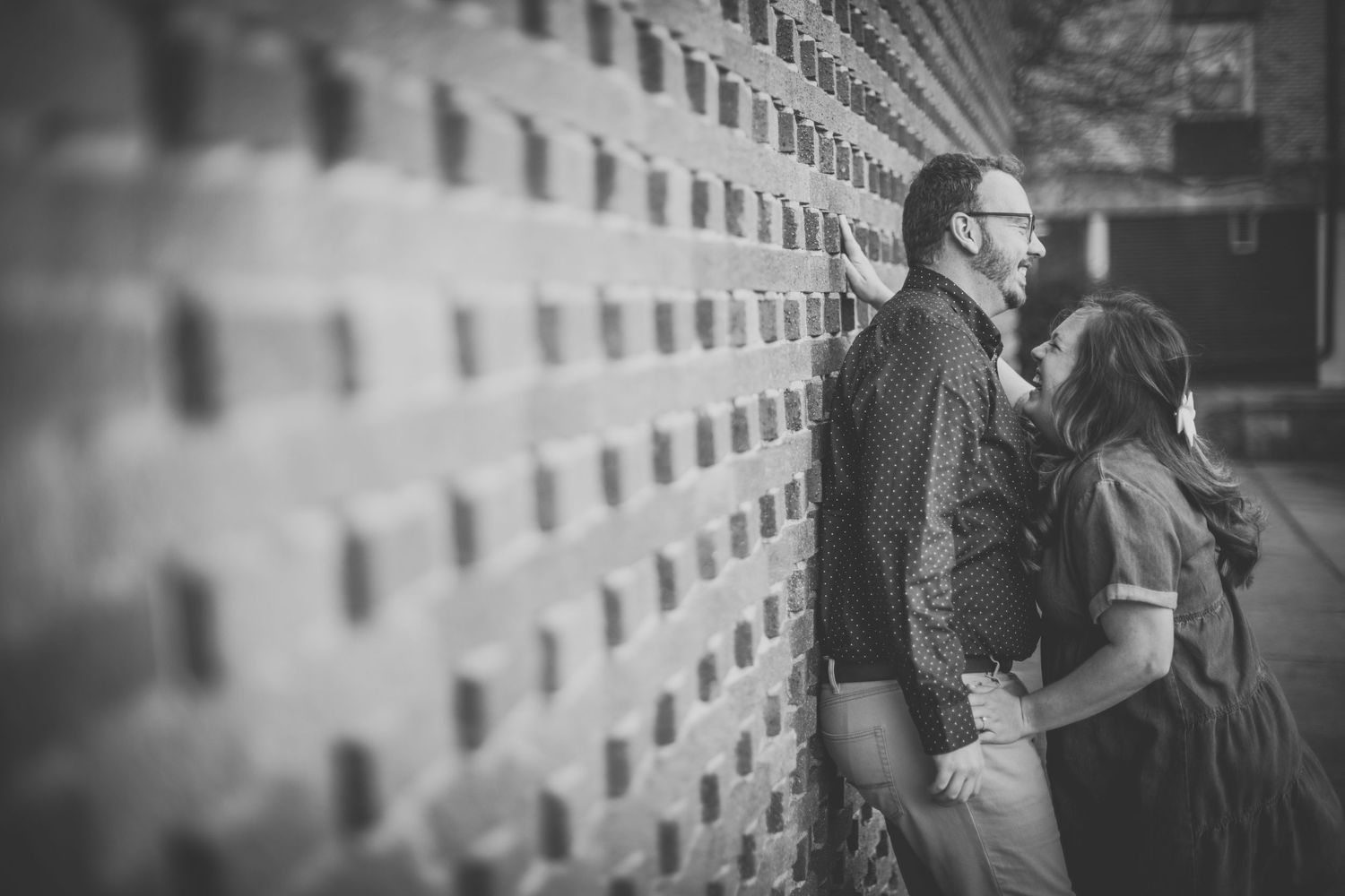 A black and white portrait of a couple sharing an intimate moment against an urban backdrop.