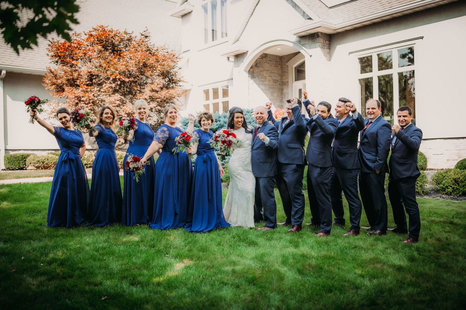 Wedding party in navy blue attire celebrates joyfully on mansion grounds.