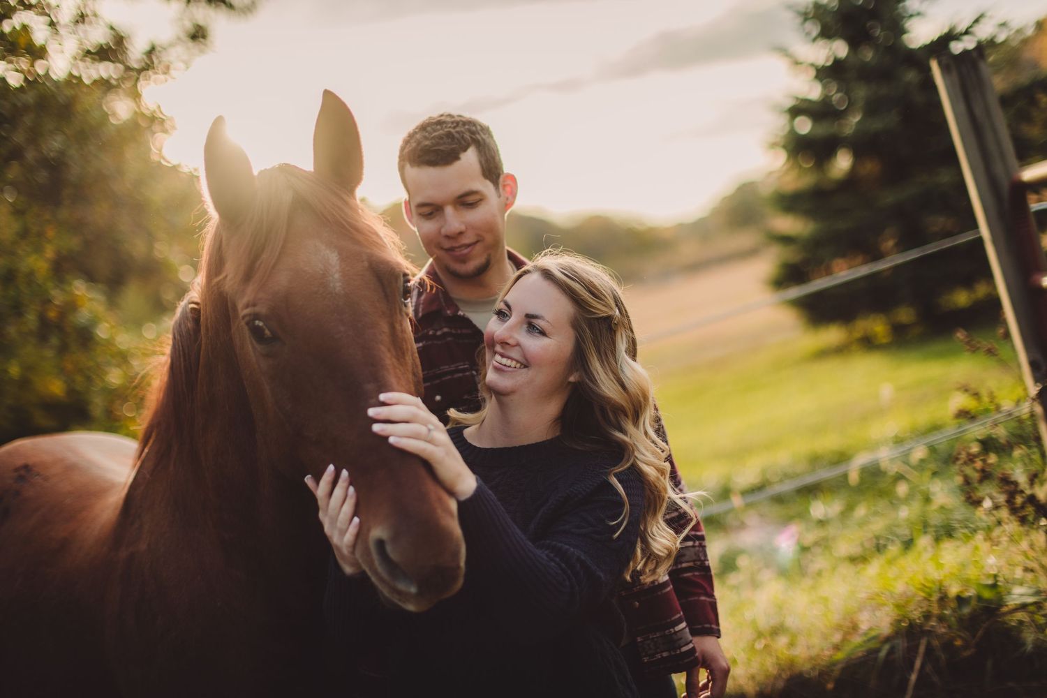 Beautiful brown horse nuzzles with two people in autumn field at sunset.