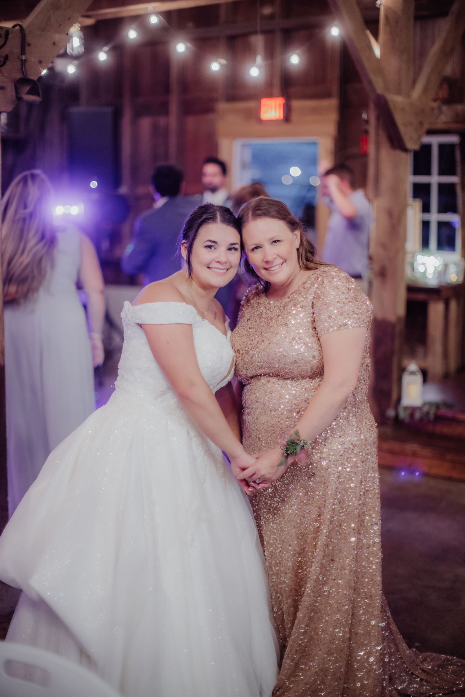Reception dancing captured in purple lighting inside a rustic barn venue.