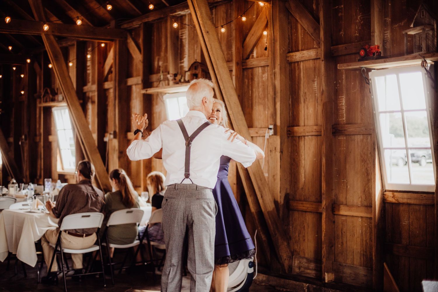 Interior of a rustic barn venue decorated with warm lighting for a wedding reception.