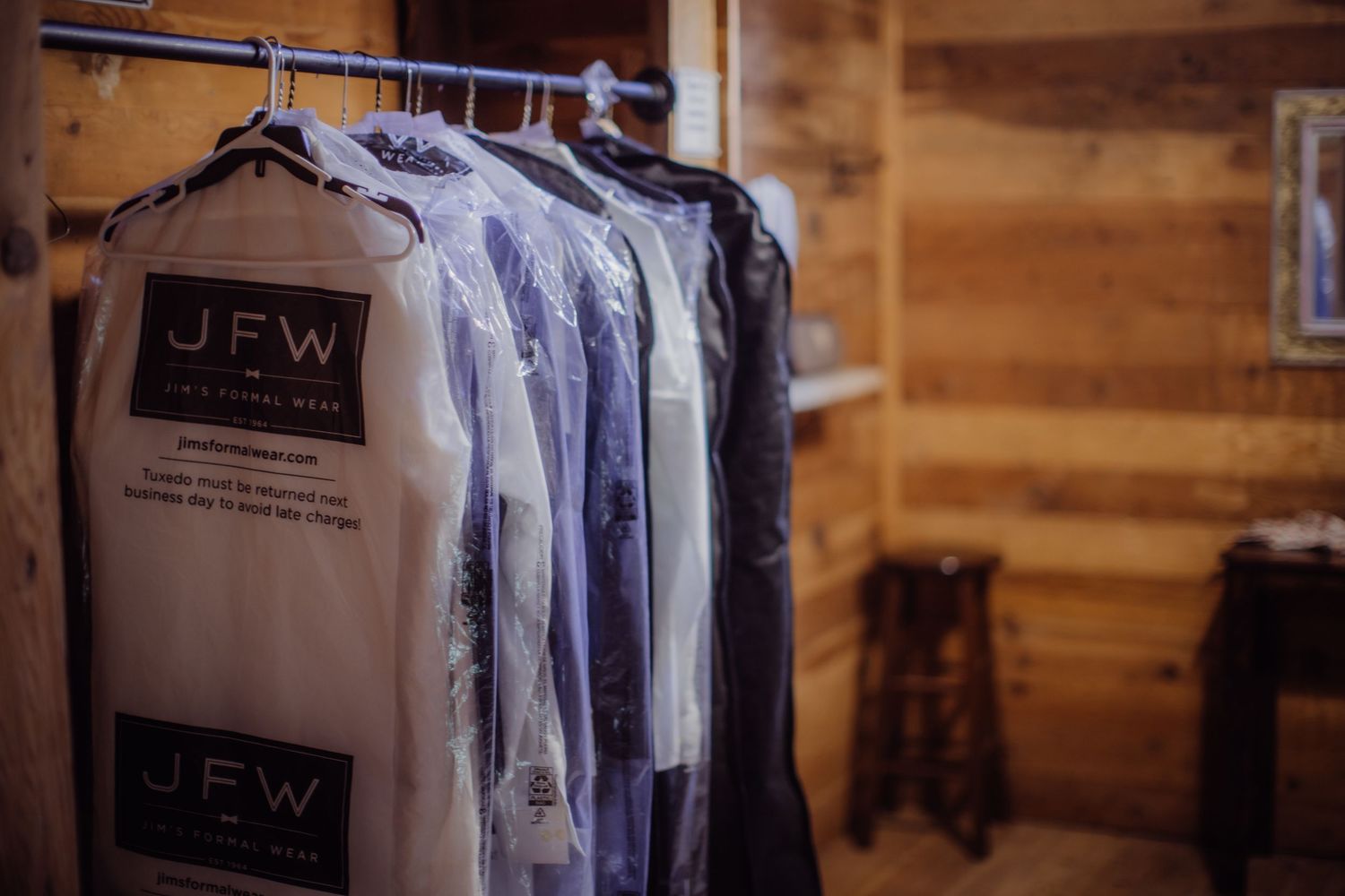 Clothing rack with formal attire hanging in wood-paneled room.