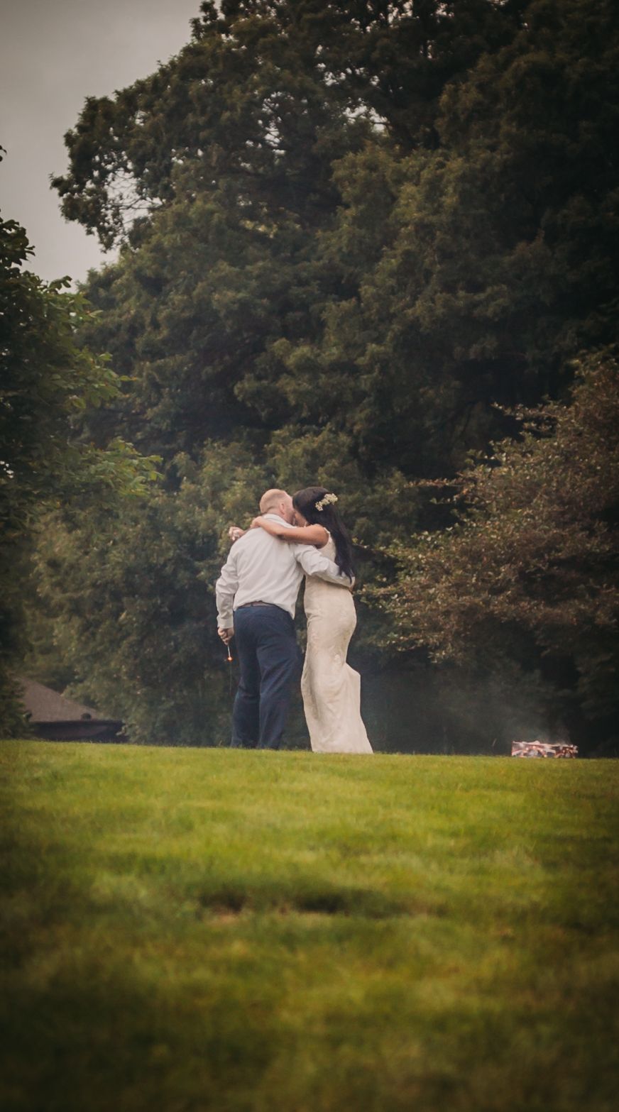 Silhouettes embrace on a serene grassy hillside during golden hour.